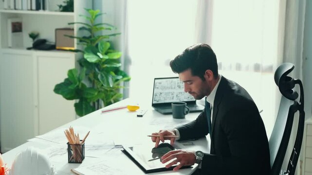 Architect engineer using laptop planning house design at office while sitting at meeting table with blueprint and equipment scatter around.Skilled civil engineer working at blueprint. Alimentation.