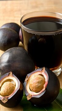 Black sapote fruit next to a glass of its rich beverage on a wooden surface
