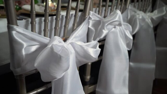 Stylishly crafted white satin bows tied onto exquisite silver chiavari chairs, creating a perfect aesthetic for weddings and elegant events that call for a touch of sophistication and beauty
