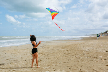 rea view of dark haired girl flying a kite on the beach