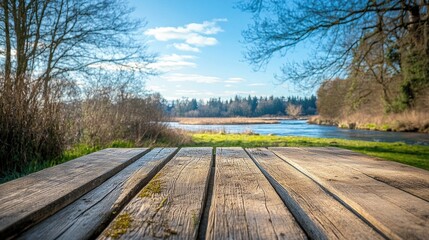 Fototapeta premium A rustic wooden table placed outdoors, surrounded by the beauty of spring, with a clear blue sky and a serene river in the background for a natural display.