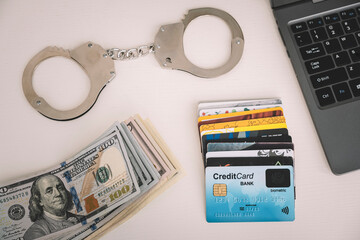 handcuffs, personal computer, cash dollars and credit cards are lying on a white table. The concept...
