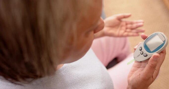 Senior woman checking blood glucose level using glucometer, focusing on health
