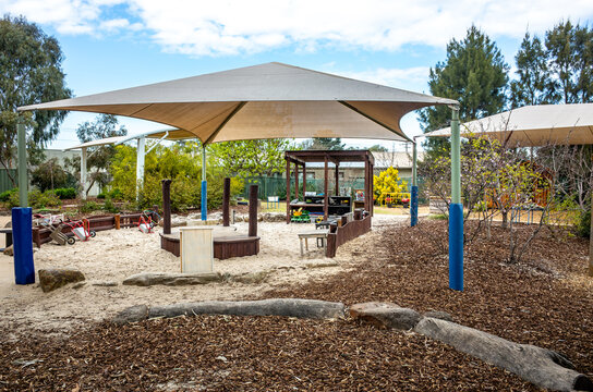 A kindergarten outdoor play area in Australia featuring a natural, safe, and engaging child-friendly environment is covered with woodchips. Shade sails are installed overhead to provide sun protection