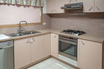 Modern L-shaped kitchen interior featuring a functional layout with a gas cooktop, built-in oven, rangehood, and sink. The essential amenities and standard fixtures in Australian residential home.