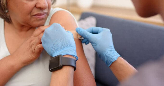 Applying bandage, healthcare worker assists senior woman after school vaccination