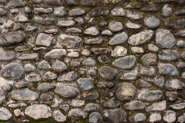 Stone masonry wall featuring textured rock surfaces. Pattern of river stones in cement. Stone wall background