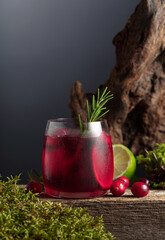 Cranberry cocktail with ice, lime, and rosemary on a old wooden board.
