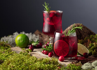 Cranberry cocktail with ice, lime, and rosemary on a old wooden board.