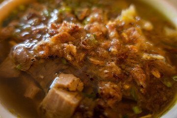 Macro shot of meat in bowl, traditional Indonesian beef soup, as well known as Soto. Indonesian Traditional Meat Soup Bowl with Flavorful Garnishes.