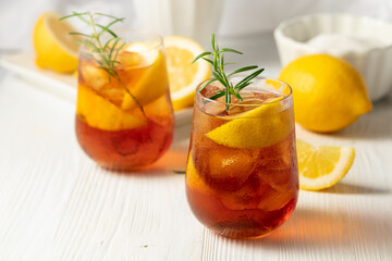 Iced tea or alcoholic cocktail with ice, rosemary and lemon slices on the white table.