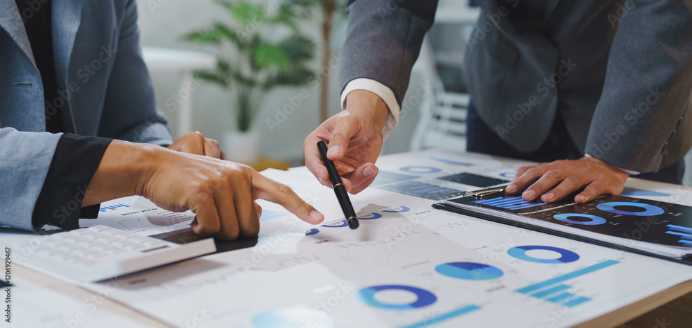 Poster two business people are pointing at financial charts and graphs spread out on a desk, using a pen an