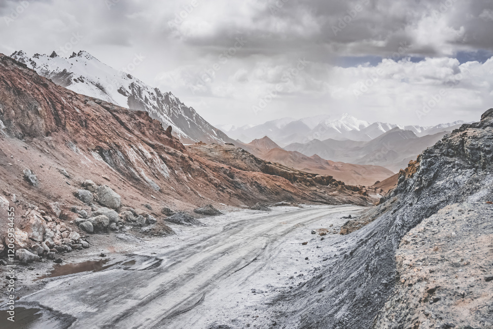 Wall mural Dusty high-mountain road of Pamir Highway and Ak-Baital Pass, panoramic landscape in rocky mountains with snow in Tien Shan Mountains in Tajikistan