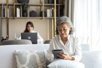 Fototapeta premium Asian senior woman using tablet for reading news, social media browsing, streaming movies and exploring health articles, modern technology for elderly lifestyle active aging with digital devices