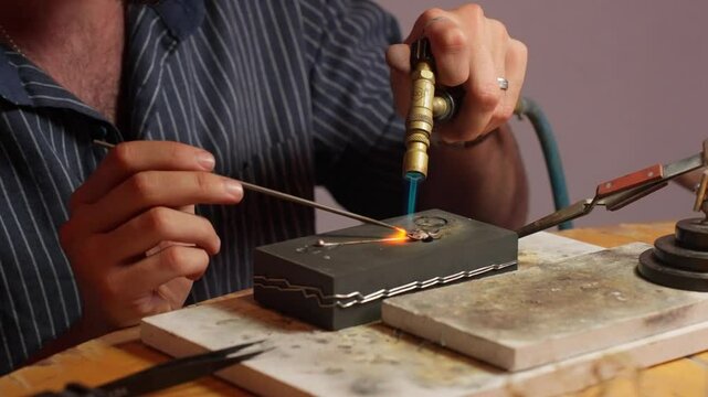 An artisan focuses on welding metal with a torch, showing expertise in jewelry making.