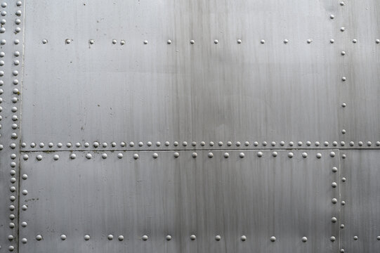 Close up of metal surface of an aircraft fuselage showing complex structure and arrangement of rivets embedded in it. Background, texture