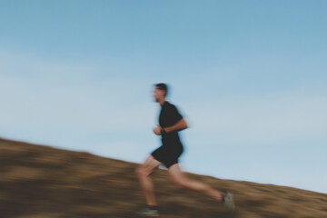 Fototapeta premium A man is running on a hill with a clear blue sky above him