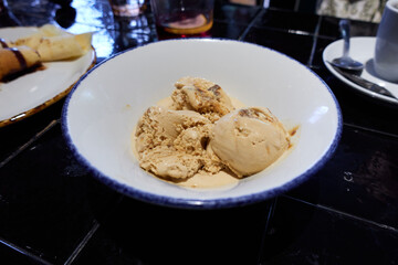 White plate with three scoops of vanilla ice cream, next to a plate with feilloas or crepes and an espresso coffee on a black table