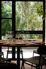 Vertical view of restaurant table prepared and empty, with unused glasses and cutlery, window with outside garden