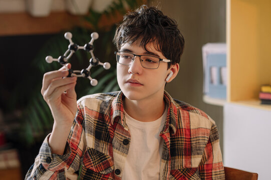 Teenage boy wearing wireless in-ear headphones examining atomic structure at home