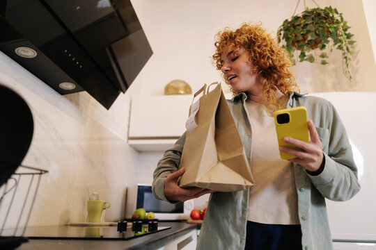 Woman holding parcel and smart phone at home