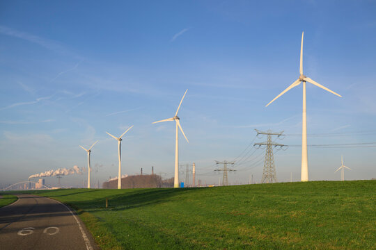 Wind turbines near grass with electricity pylon under blue sky