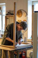 Joiner assembles table, attaching legs to base in wood store workshop. Male with screwdriver making...