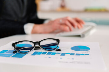 Eyeglasses over bar graph diagram with businesswoman working in background at office