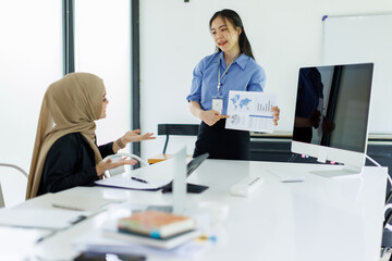 Young businesswoman adviser standing in front of laptop and giving advise to sales woman. Business people consulting at office. asian teamwork concept.
