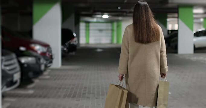 Young woman walks through the parking lot of shopping center to car. Puts paper bags with purchases. Shopping, sale, discounts in stores.