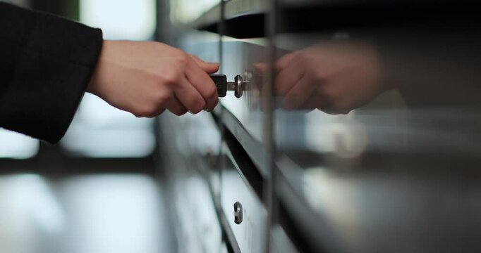 Close-up woman is opening her mailbox inside a cluster of mailboxes for her apartment. Mail shipping concept.