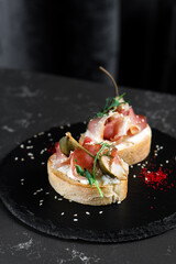 Bruschetta two pieces with dried meat and sauce on a black plate