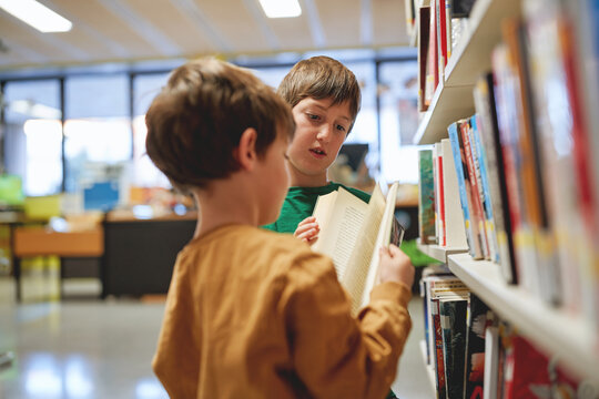 Two boys reading a book together in a library.