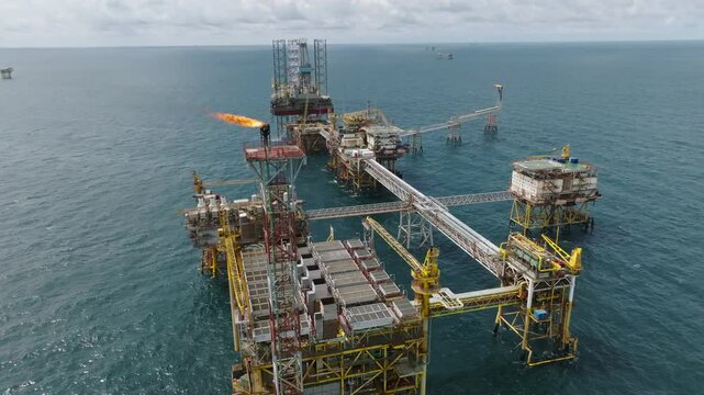 Sweeping aerial of huge offshore processing platform with multiple gas flares, oil industry
