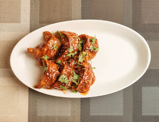 Spicy fried momos coated in flavorful sauce, garnished with sesame seeds and fresh coriander. A delicious Asian street food snack served on a white plate, perfect for restaurant menus and food blogs