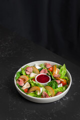Salad of fresh vegetables and greens with red sauce on a dark table