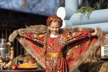 A blonde girl in a national Russian costume on the Maslenitsa holiday. A beautiful russian girl in a national costume made of a fur cape and kokoshnik on the background of a hayloft. 
