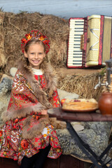 A blonde girl in a national Russian costume on the Maslenitsa holiday. A beautiful russian girl in a national costume made of a fur cape and kokoshnik on the background of a hayloft. 