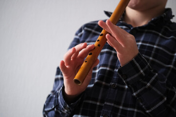 A child playing a wooden reed pipe, showcasing skill and concentration on a gray background, angle of view from below © HalynaRom