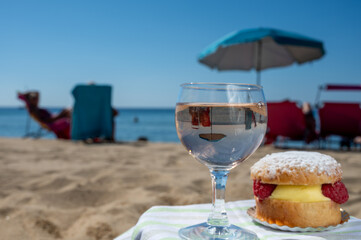 Lunch on sandy beach in Saint-Tropez with cake Tarte tropezienne filled brioche with cream and fresh red berries and glass of rose wine, summer vacation on French riviera, France
