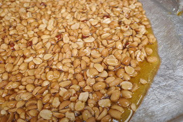 A tray of peanuts in syrup made from sugar that has been simmered over heat, prepare for to be pounded.  Pound quickly until the peanuts and sugar are well blended. 