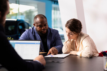 Customers in showroom completing credit application and financing paperwork after deciding to purchase new car. Salesman in dealership discussing financing options with clients