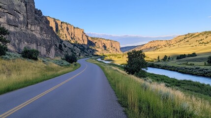 Scenic winding road alongside a river, framed by cliffs and lush greenery.