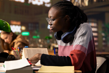 African american college student writes her bachelor degree paper, surrounded by reference books and reliable university study materials. Girl collecting notes and citations for her diploma.