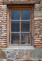 Weathered wooden window framed by rustic stone wall in historical building