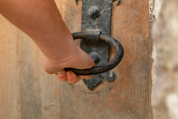Hand gripping an antique door knocker on a rustic wooden door