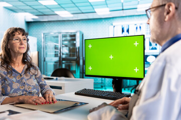 Senior physician consulting old lady next to mockup display in the cabinet, discussing about medicine and a treatment plan for wellness. Experienced medic gives advice and support to his patient.