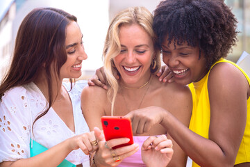 Three joyful young women shopping and looking at a smartphone together.