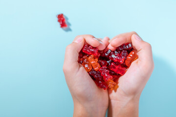 Vitamins and supplements for child, gummy bears in kids hands.  Flat lay. Blue background