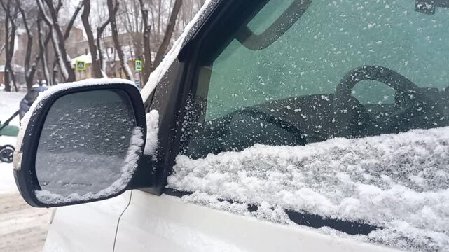 snow-covered side rear view mirror of a minivan by light falling snow in inclement snowy weather